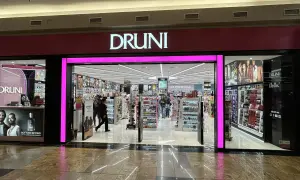 Fachada de tienda **Druni** con iluminación rosa brillante y el logo en blanco. Dentro, estanterías llenas de productos de belleza y perfumes.