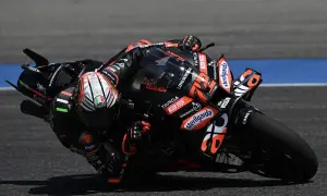Motociclista de MotoGP inclinado en una curva, con su moto negra y naranja.