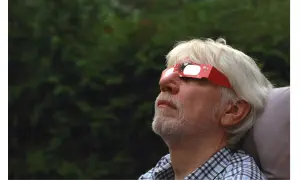 Hombre mayor con barba blanca mira al cielo con gafas eclipse solar rojas, disfrutando del fenómeno.