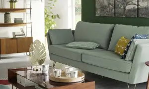 Sofá verde menta con cojines decorativos y una mesita de centro de cristal, estilo La Redoute.