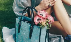 Un bolso de mezclilla azul con tachuelas y asas negras, adornado con un ramo de anémonas rosadas.