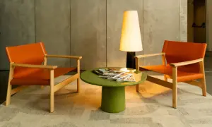 Dos sillones naranjas de Kave Home flanquean una mesa verde con revistas. Una lámpara alta ilumina la escena.