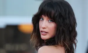 Mujer con cabello oscuro y ondulado, peinado en capas estilo corte mariposa, mira a la cámara con ojos azules penetrantes.