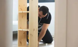Hombre montando un estante de madera, estilo IKEA.