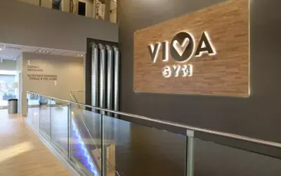 Letrero luminoso "VIVA GYM" sobre pared de madera. Escaleras con luces azules y barandilla de cristal.