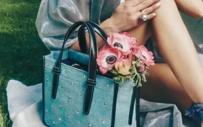 Un bolso de mezclilla azul con tachuelas y asas negras, adornado con un ramo de anémonas rosadas.