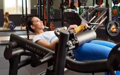 Mujer sonriente realiza un hip thrust en máquina de gimnasio, concentrada en el ejercicio para fortalecer glúteos.