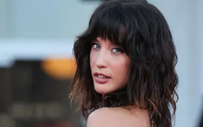 Mujer con cabello oscuro y ondulado, peinado en capas estilo corte mariposa, mira a la cámara con ojos azules penetrantes.