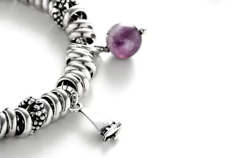 Pulsera de plata con charms, destacando una cuenta de amatista púrpura y un charm en forma de campana.