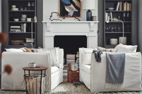 Salón acogedor de Ikea España con sofás blancos, chimenea y estanterías llenas de libros y objetos decorativos.