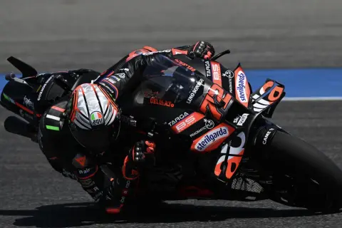 Motociclista de MotoGP inclinado en una curva, con su moto negra y naranja.