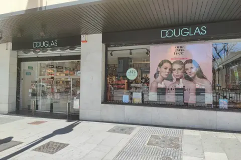 Fachada de tienda Douglas con un anuncio de tres modelos y el lema "one. two. free!".
