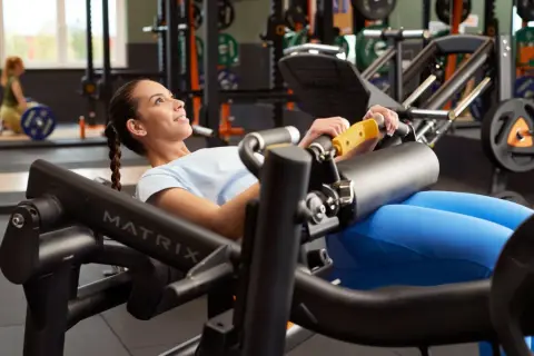 Mujer sonriente realiza un hip thrust en máquina de gimnasio, concentrada en el ejercicio para fortalecer glúteos.
