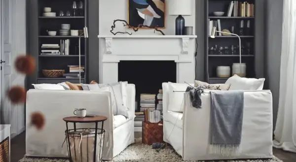 Salón acogedor de Ikea España con sofás blancos, chimenea y estanterías llenas de libros y objetos decorativos.