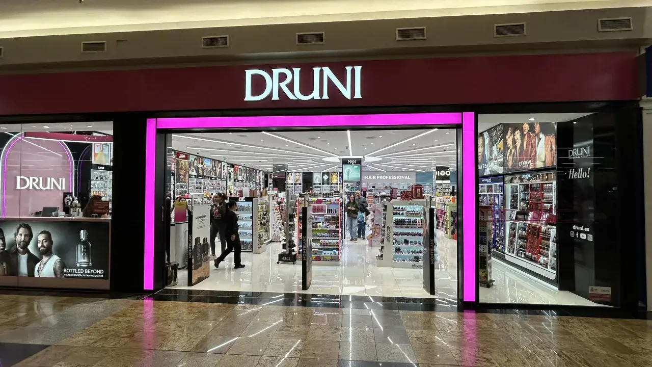 Fachada de tienda **Druni** con iluminación rosa brillante y el logo en blanco. Dentro, estanterías llenas de productos de belleza y perfumes.