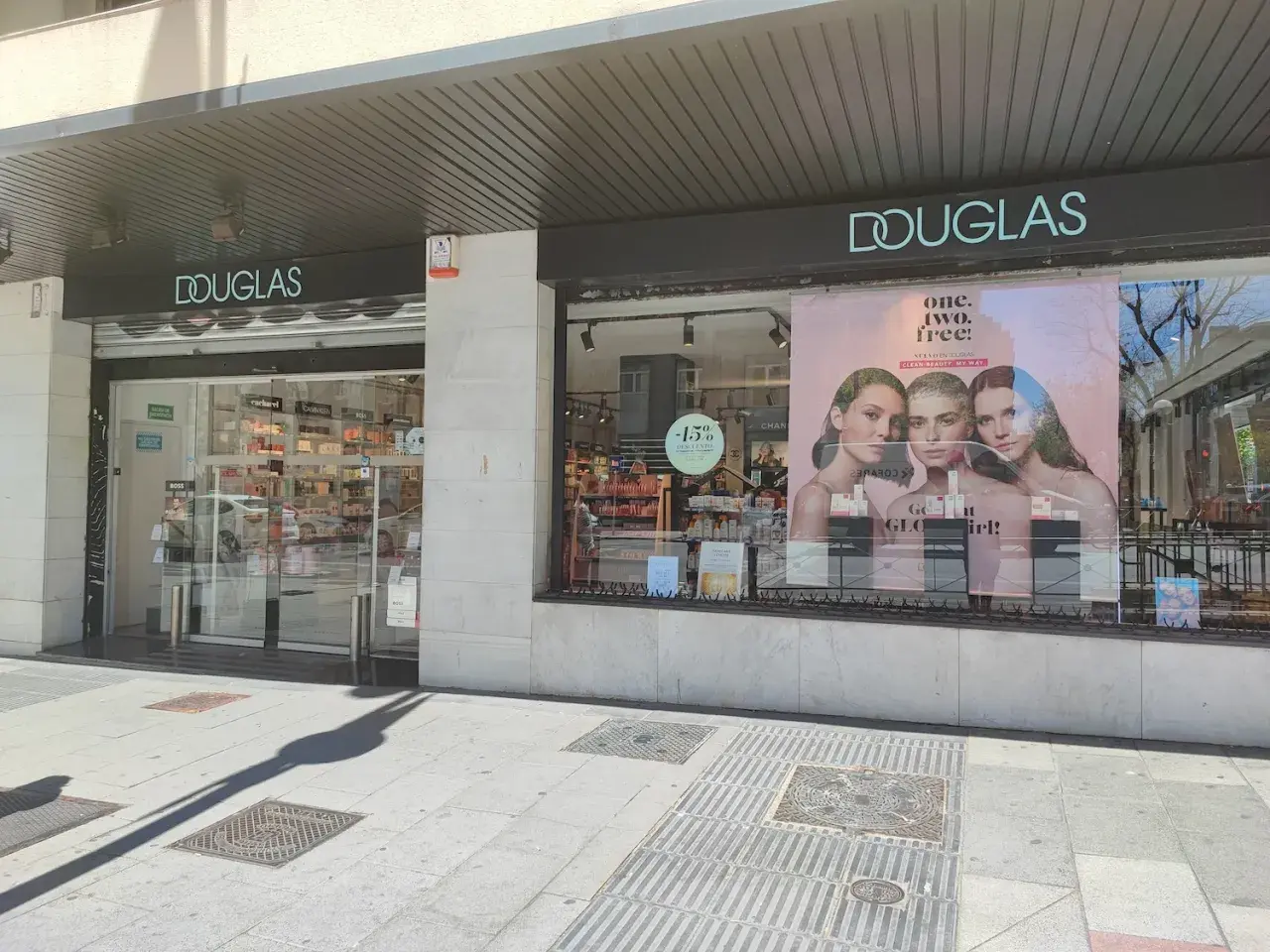 Fachada de tienda Douglas con un anuncio de tres modelos y el lema "one. two. free!".