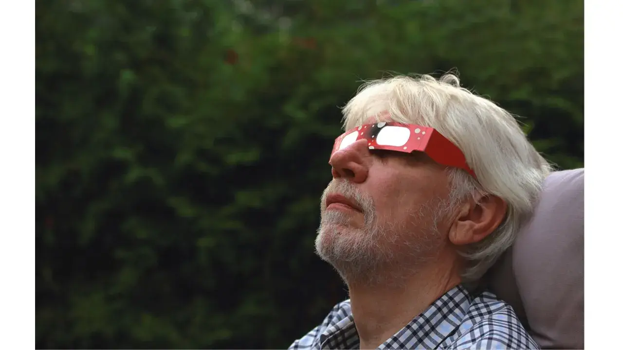 Hombre mayor con barba blanca mira al cielo con gafas eclipse solar rojas, disfrutando del fenómeno.