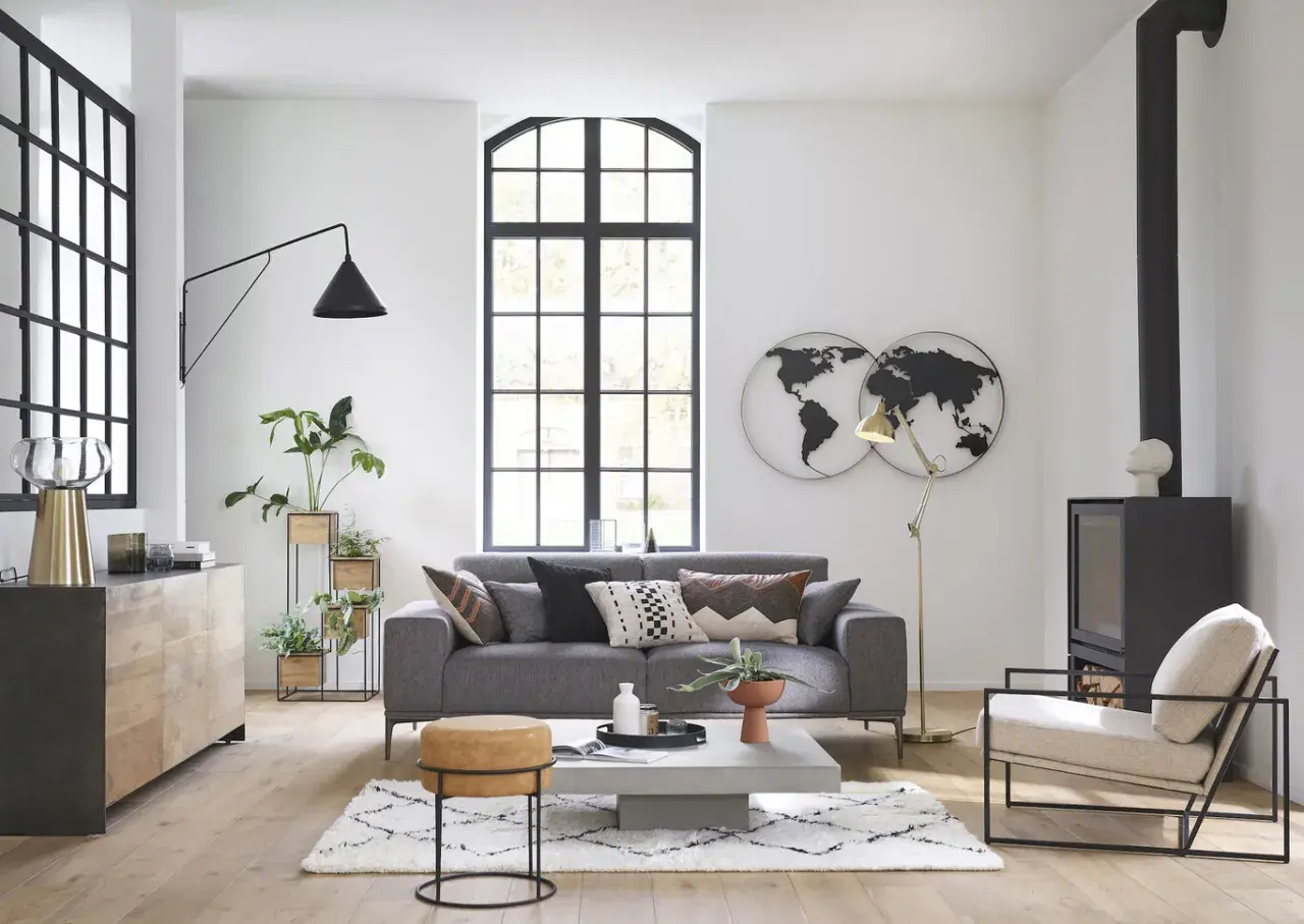 Salón moderno con sofá gris, mesa de centro, chimenea y decoración de mapas del mundo, estilo Maison du Monde.