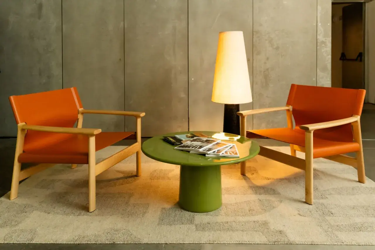 Dos sillones naranjas de Kave Home flanquean una mesa verde con revistas. Una lámpara alta ilumina la escena.