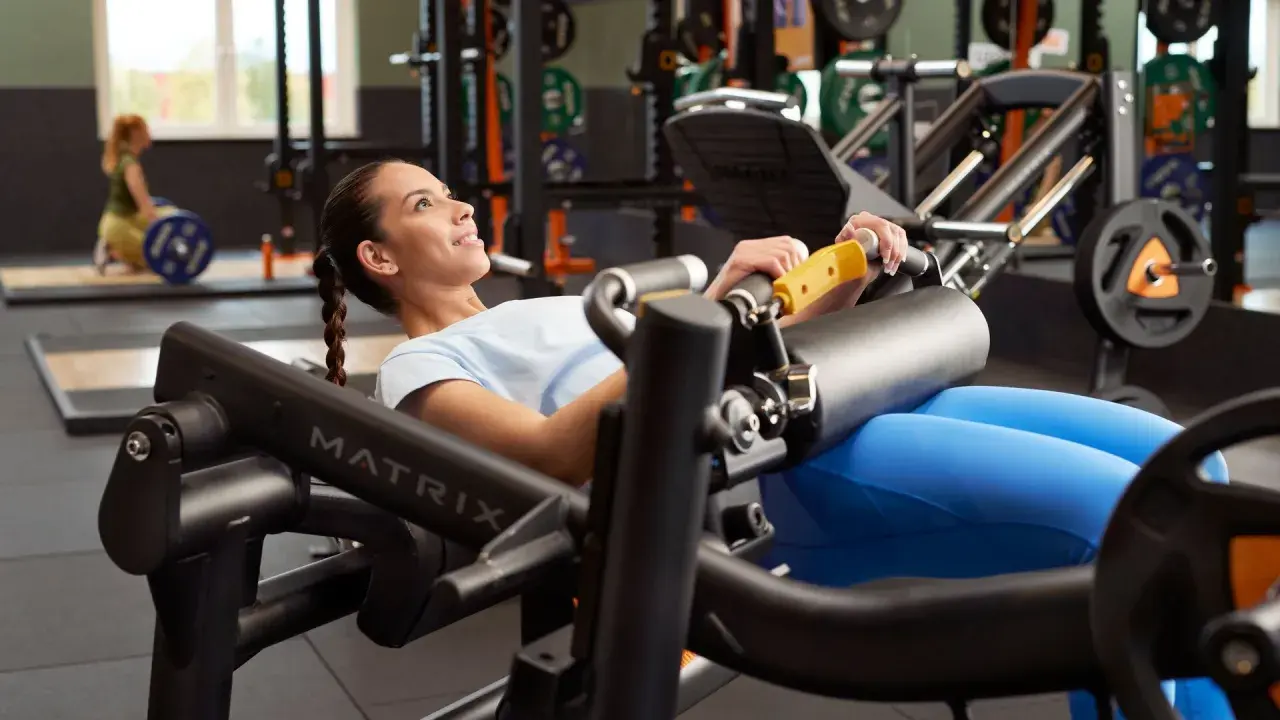 Mujer sonriente realiza un hip thrust en máquina de gimnasio, concentrada en el ejercicio para fortalecer glúteos.
