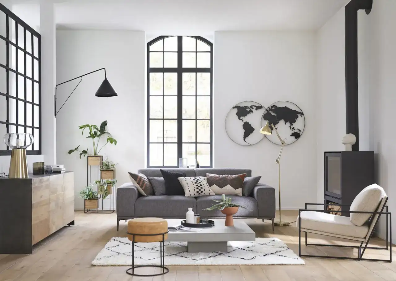 Salón moderno con sofá gris, mesa de centro, chimenea y decoración de mapas del mundo, estilo Maison du Monde.