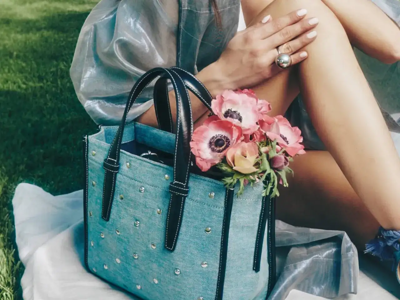 Un bolso de mezclilla azul con tachuelas y asas negras, adornado con un ramo de anémonas rosadas.