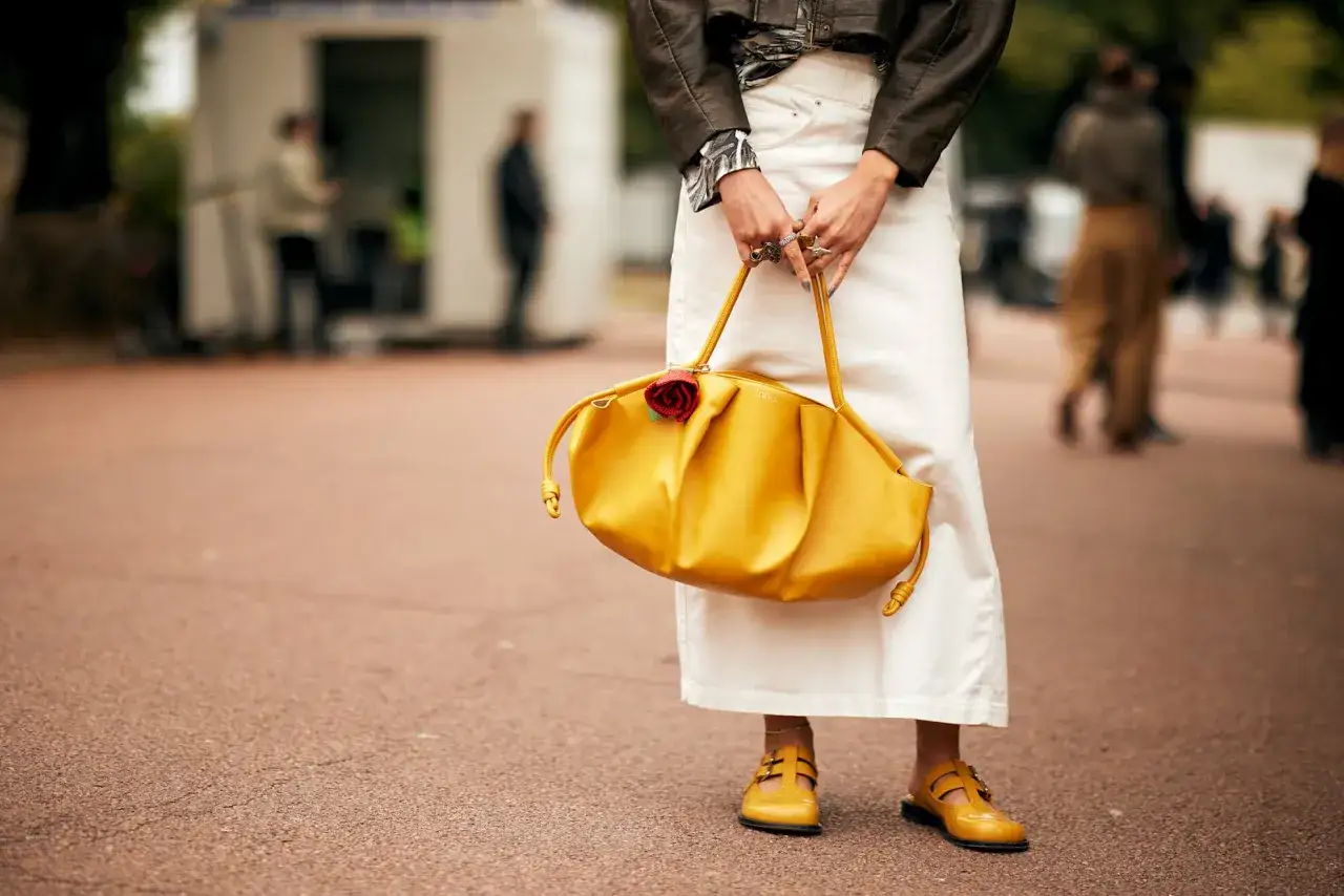 Una mujer sostiene un bolso amarillo vibrante con un detalle de rosa roja. Sus zapatos amarillos a juego complementan este accesorio de moda.