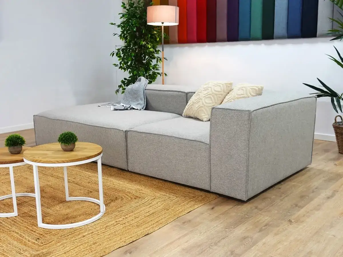 Sofá modular gris con cojines y manta, mesas auxiliares de madera y alfombra de yute, estilo IKEA.