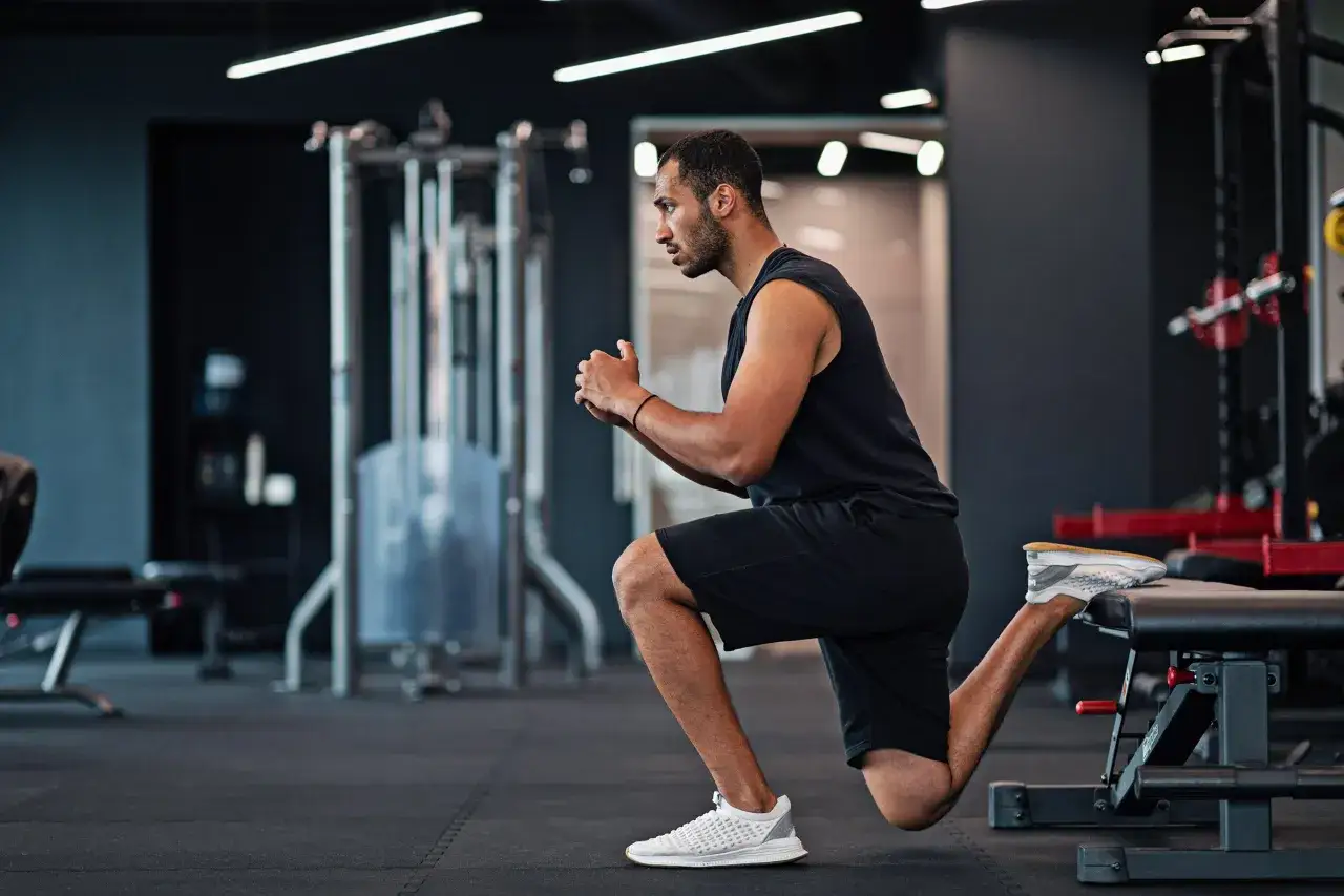 Hombre concentrado realizando una sentadilla búlgara en un gimnasio moderno.
