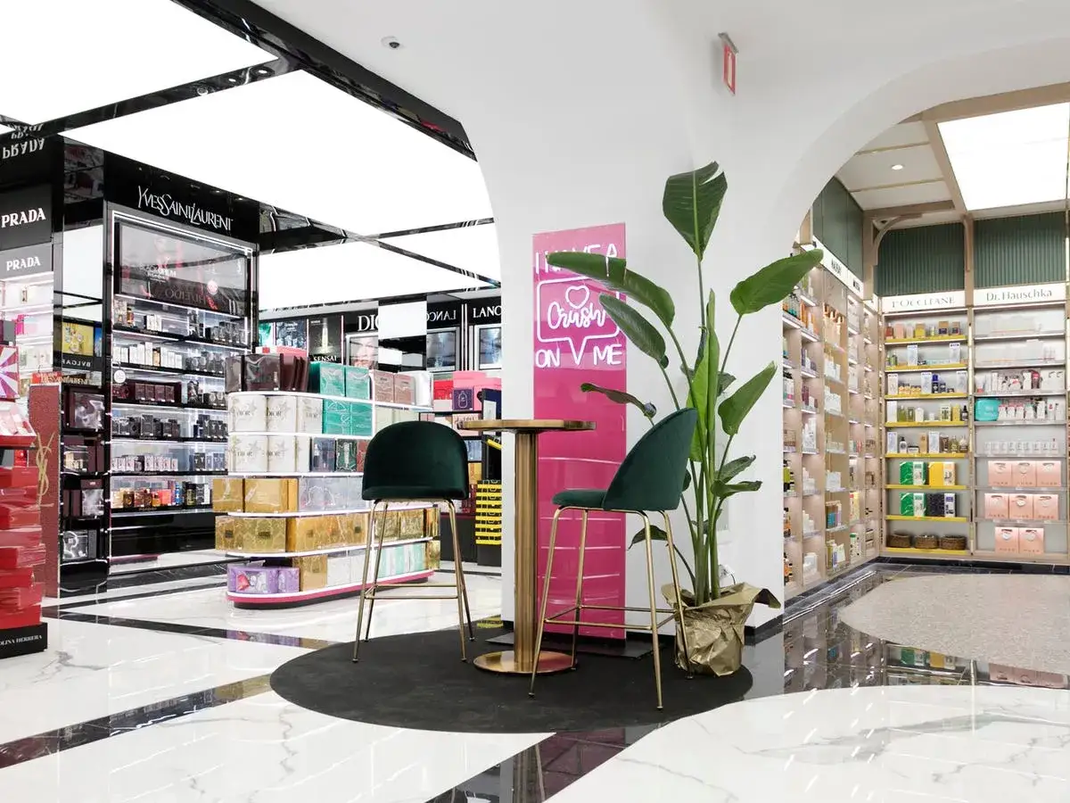 Interior de una tienda Druni con estanterías de perfumes y cosméticos, plantas y un rincón para sentarse.