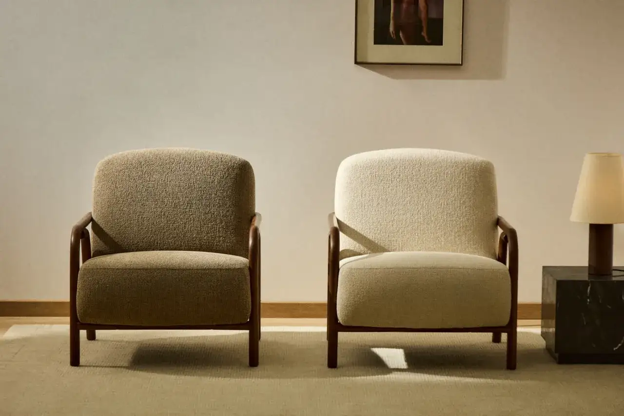 Dos sillones de Kave Home, uno beige y otro crema, con estructura de madera. Un cuadro y una lámpara completan la escena.