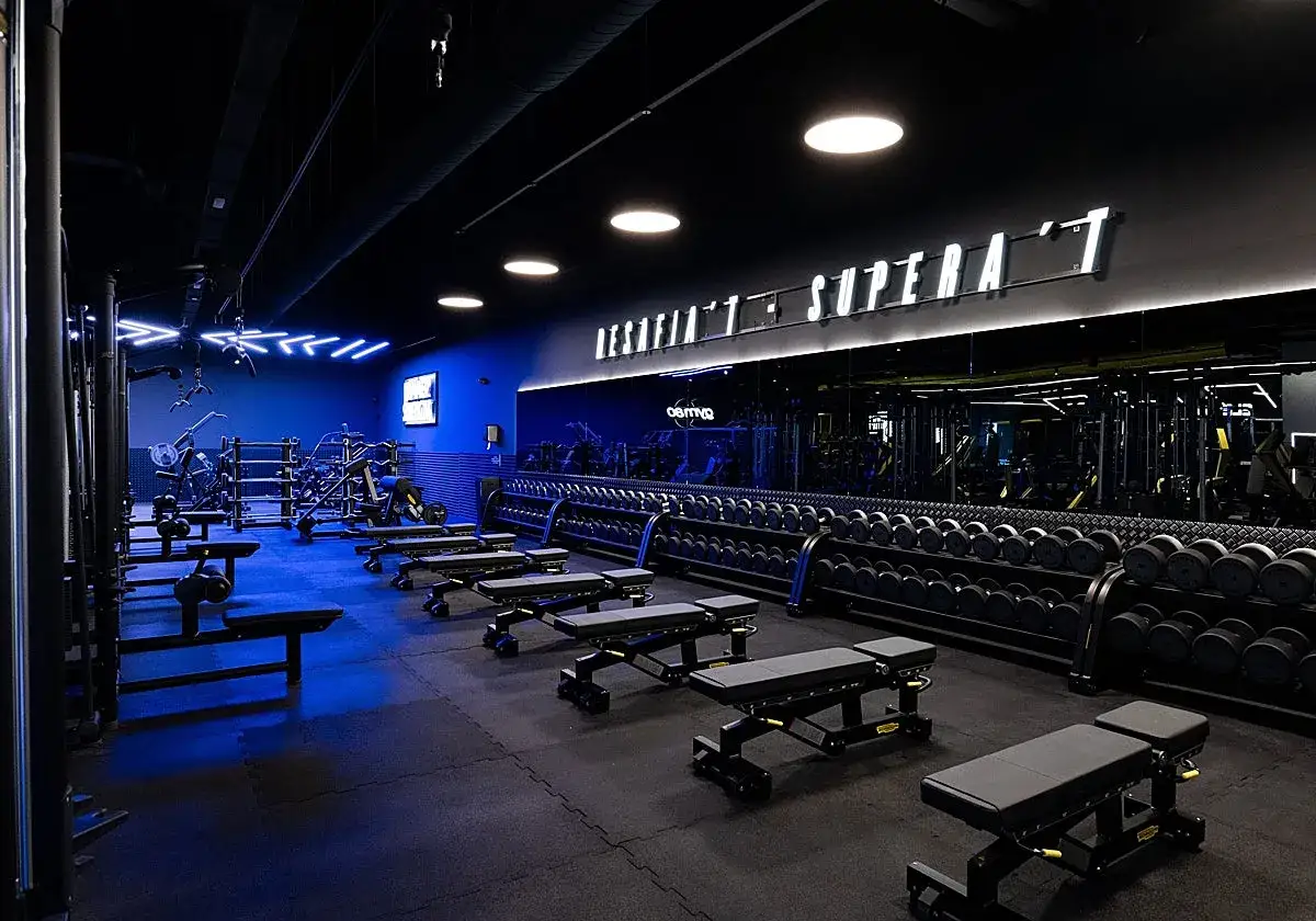 Moderno fitness park con pesas, bancos y máquinas. Iluminación azul y letrero luminoso