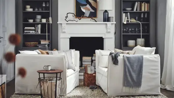 Salón acogedor de Ikea España con sofás blancos, chimenea y estanterías llenas de libros y objetos decorativos.