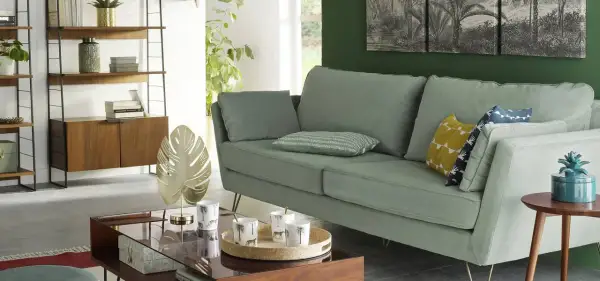 Sofá verde menta con cojines decorativos y una mesita de centro de cristal, estilo La Redoute.