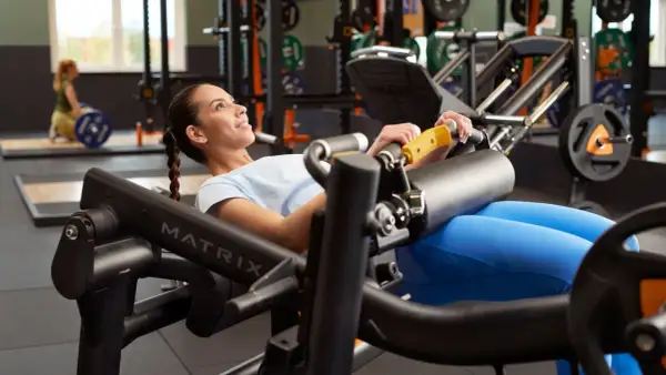 Mujer sonriente realiza un hip thrust en máquina de gimnasio, concentrada en el ejercicio para fortalecer glúteos.